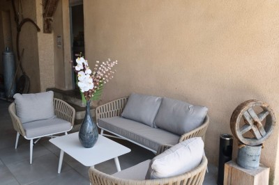 Grande maison en pierre entourée de verdure, avec une cour ensoleillée et des arbres en arrière-plan.