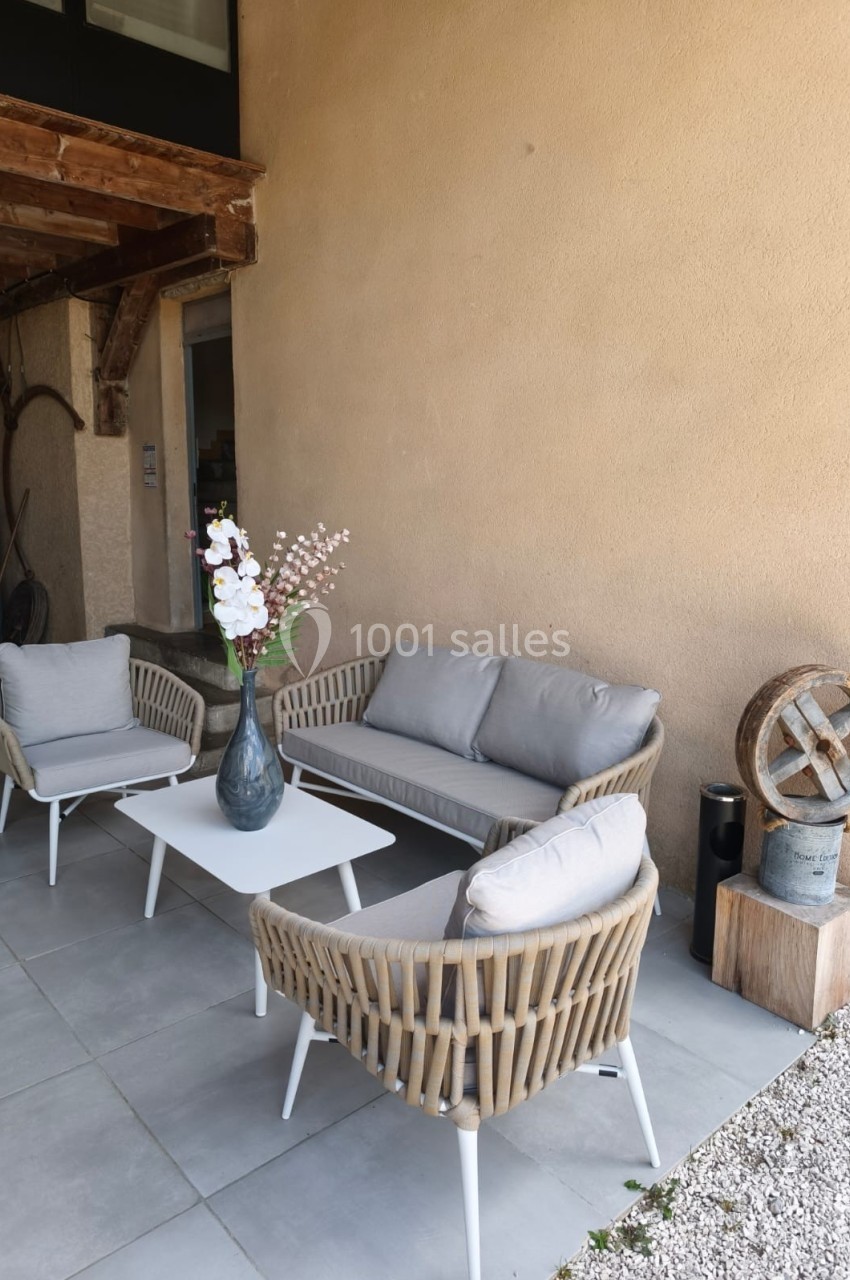 Salon de jardin avec canapé, fauteuils en rotin et table basse blanche, disposé sur une terrasse en carrelage gris.