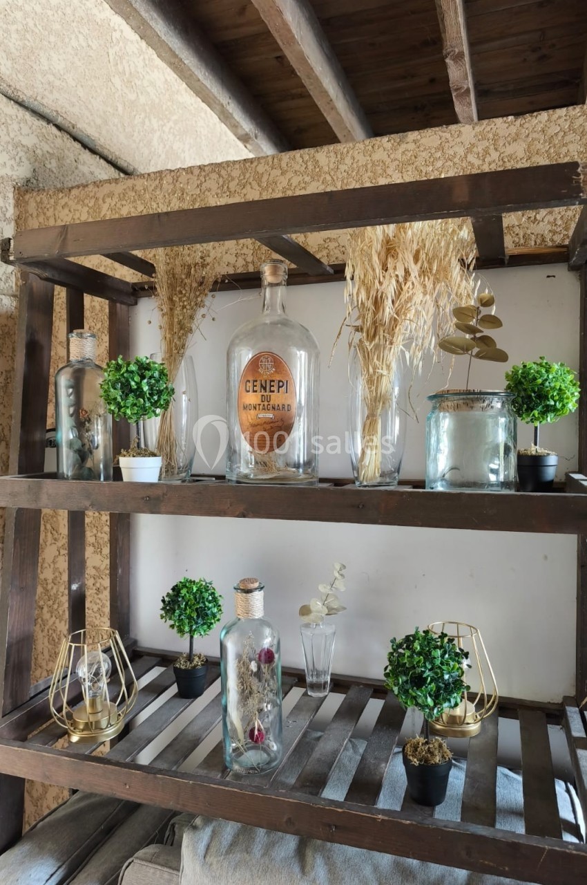 Étagère en bois décorée de plantes, bouteilles en verre, épis de blé séchés et objets décoratifs dans un intérieur rustique.