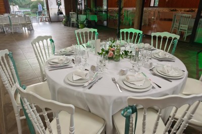 Grande maison en pierre entourée de verdure, avec une cour ensoleillée et des arbres en arrière-plan.