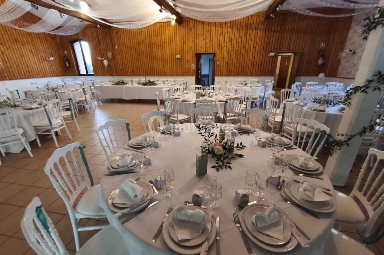 Salle de réception décorée pour un mariage, avec tables rondes dressées, nappes blanches et compositions florales.