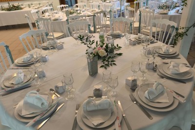 Grande maison en pierre entourée de verdure, avec une cour ensoleillée et des arbres en arrière-plan.