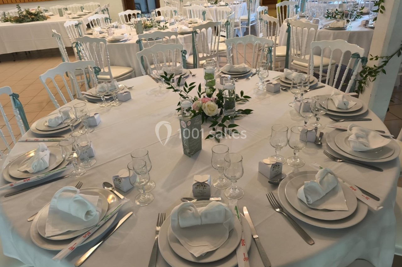 Table ronde élégamment dressée avec nappes blanches, vaisselle raffinée et décoration florale au centre.
