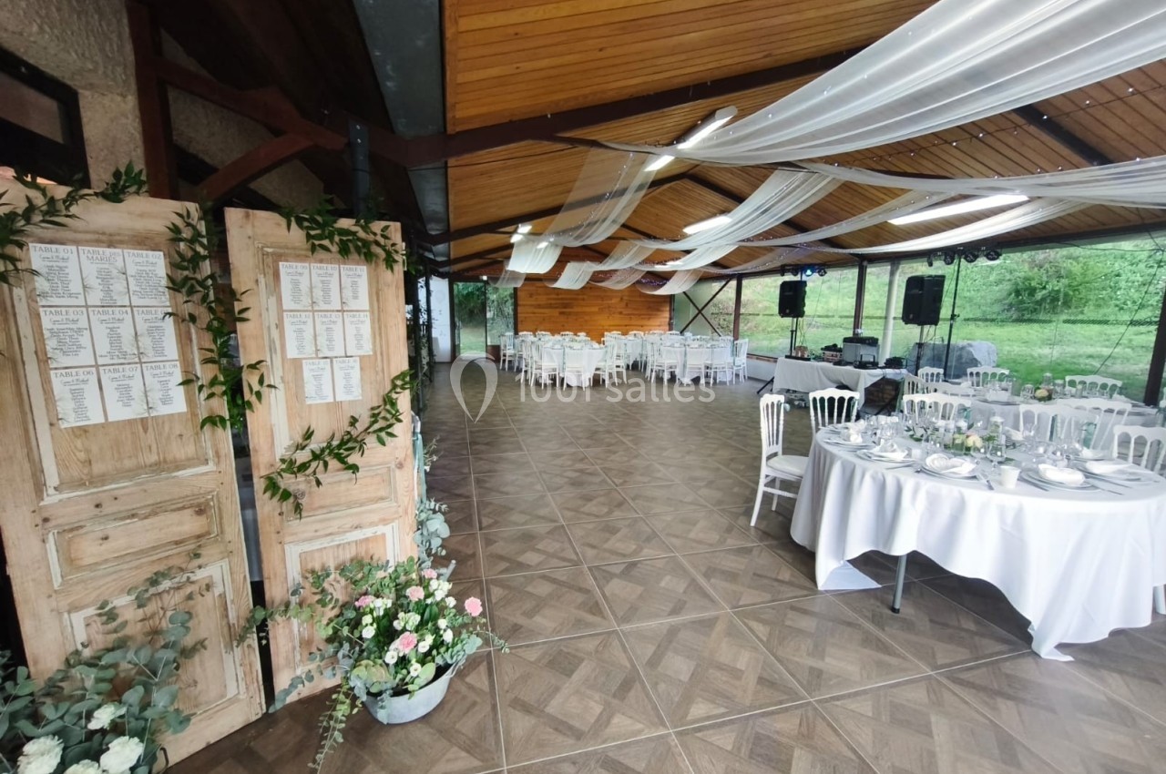 Salle de réception décorée avec des tables dressées, des chaises blanches et des voilages suspendus au plafond.