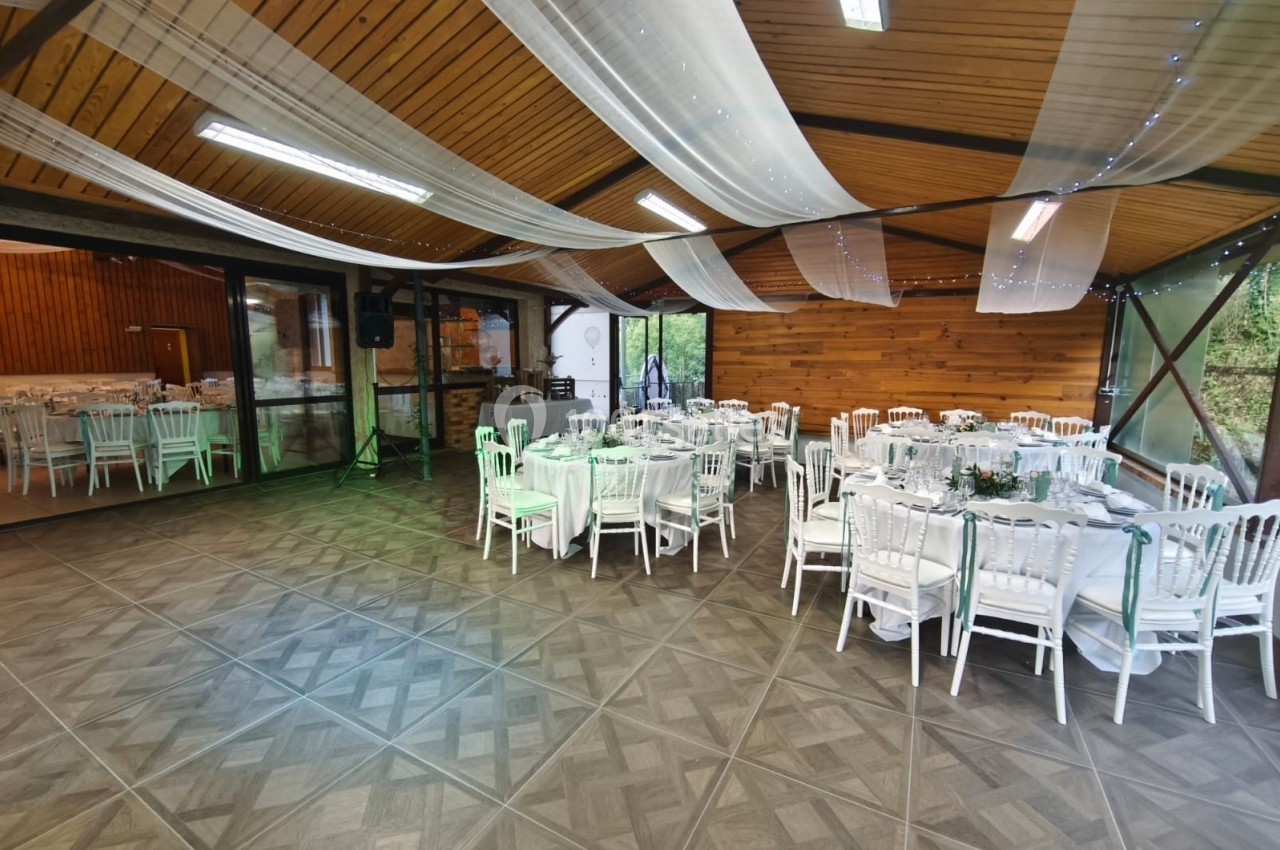 Salle de réception décorée avec des tables rondes dressées, chaises blanches et voilages suspendus au plafond.