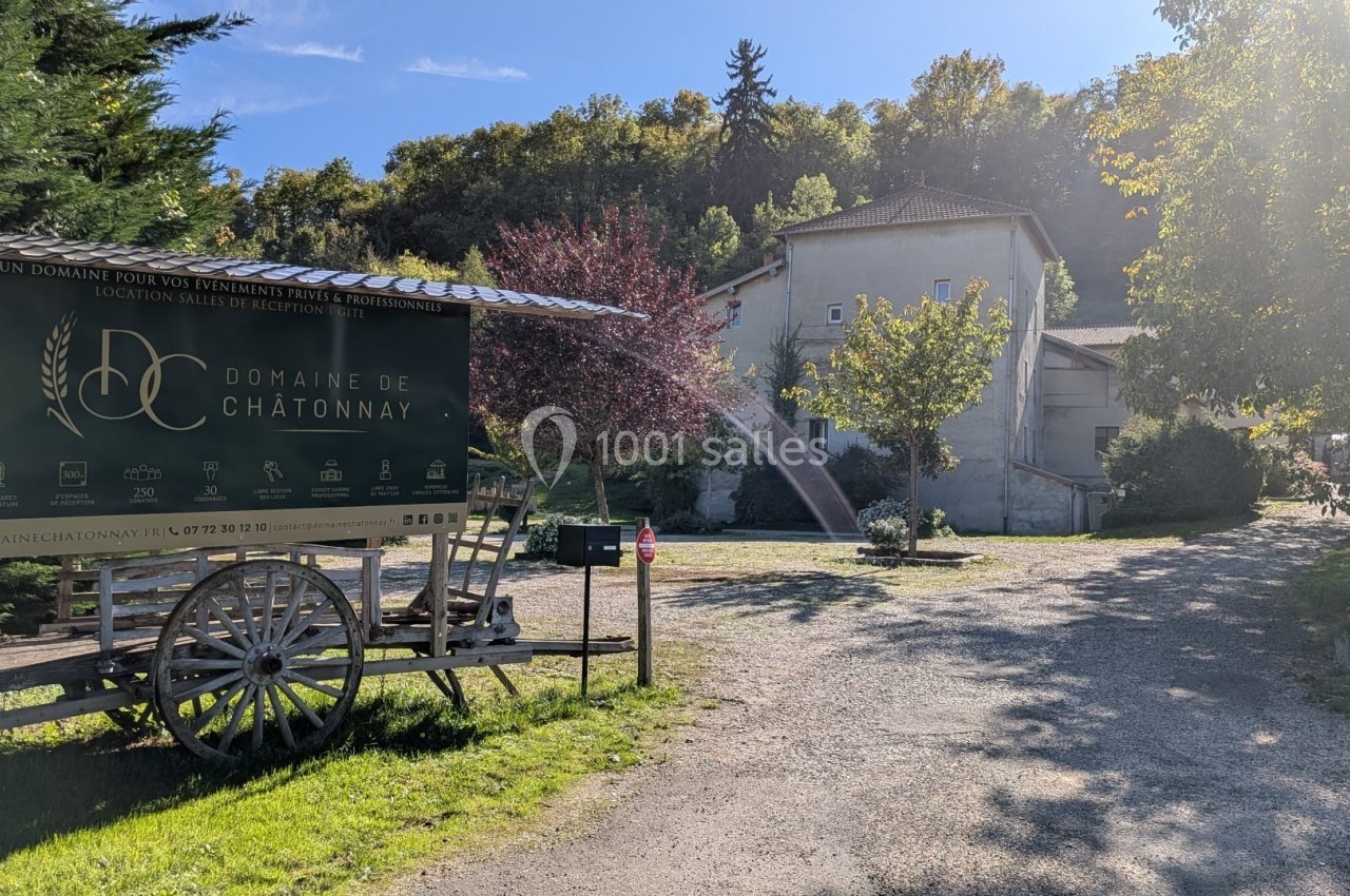 Panneau du Domaine de Châtonnay sur une charrette en bois, devant un chemin menant à des bâtiments entourés de verdure.