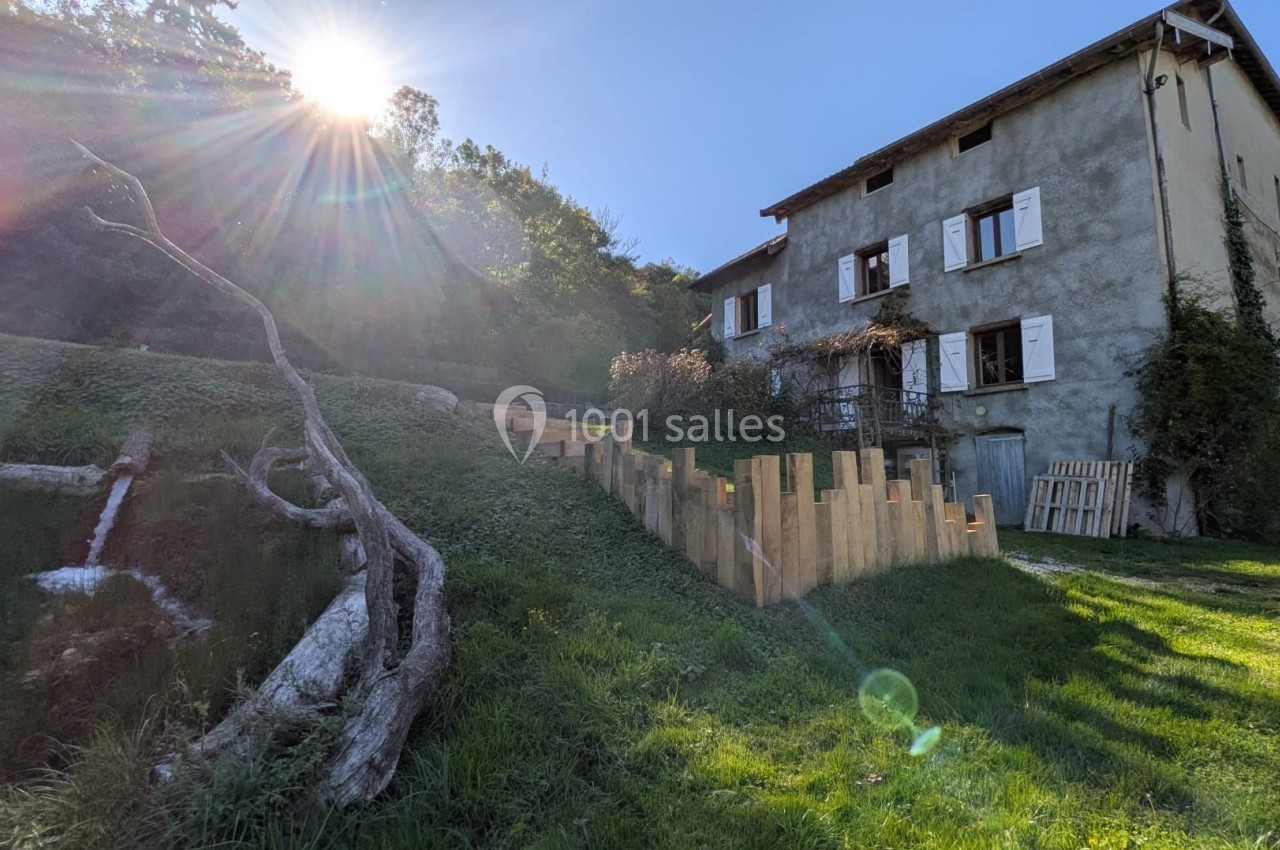 Maison en pierre avec volets blancs, située sur un terrain en pente avec un escalier en bois et un arbre tombé.