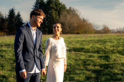 Un couple en tenue de mariage pose dans un champ au coucher du soleil, la mariée tenant un bouquet de fleurs blanches.