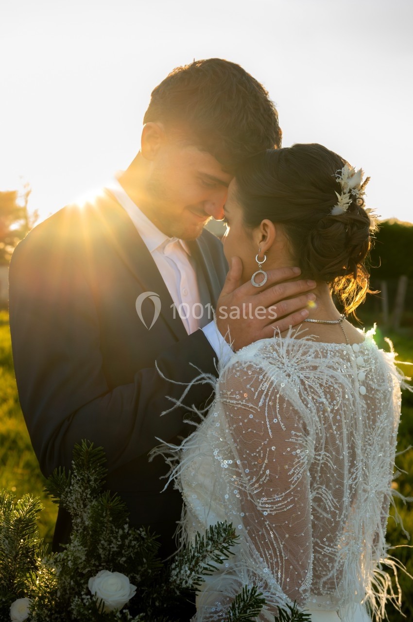 Un couple en tenue de mariage s'enlace tendrement dans un champ au coucher du soleil.