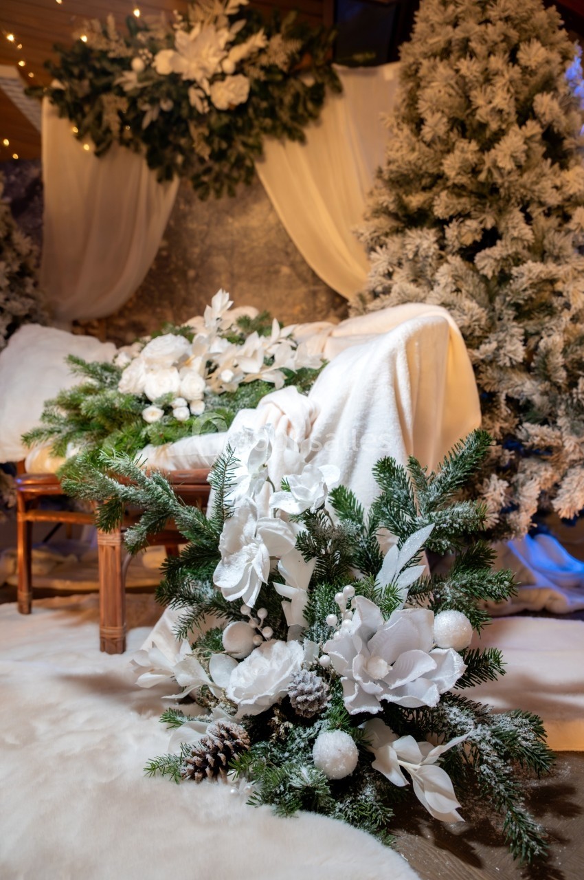 Décoration hivernale avec sapins enneigés, guirlandes lumineuses et compositions florales blanches sur fond chaleureux.