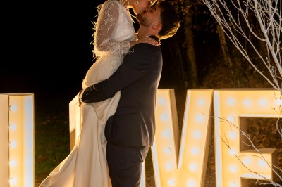 Un couple en tenue de mariage pose dans un champ au coucher du soleil, la mariée tenant un bouquet de fleurs blanches.