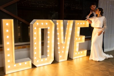 Un couple en tenue de mariage pose dans un champ au coucher du soleil, la mariée tenant un bouquet de fleurs blanches.