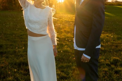 Un couple en tenue de mariage pose dans un champ au coucher du soleil, la mariée tenant un bouquet de fleurs blanches.