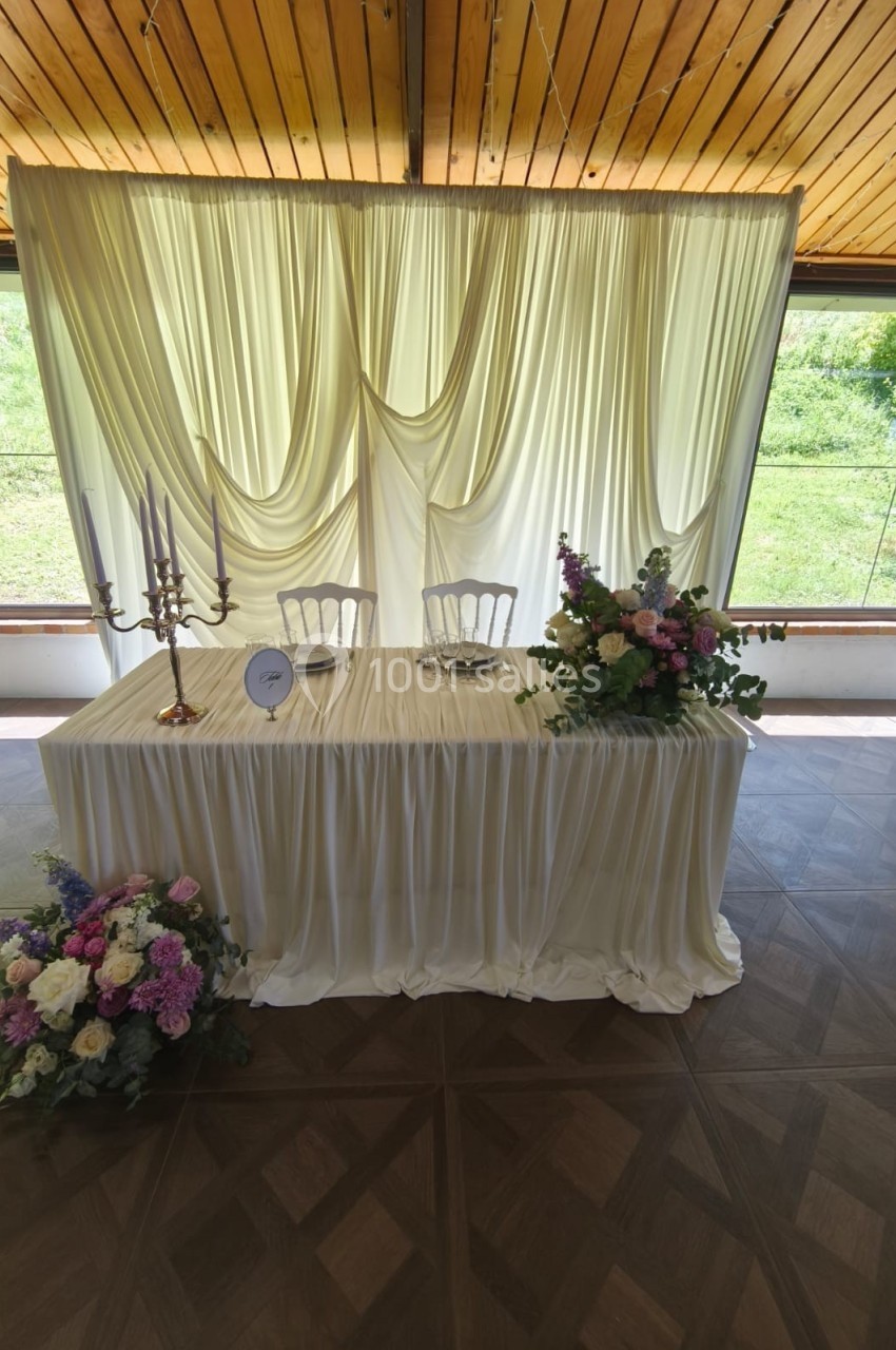 Table décorée pour un mariage avec nappes blanches, chandeliers, fleurs colorées et rideaux en arrière-plan.