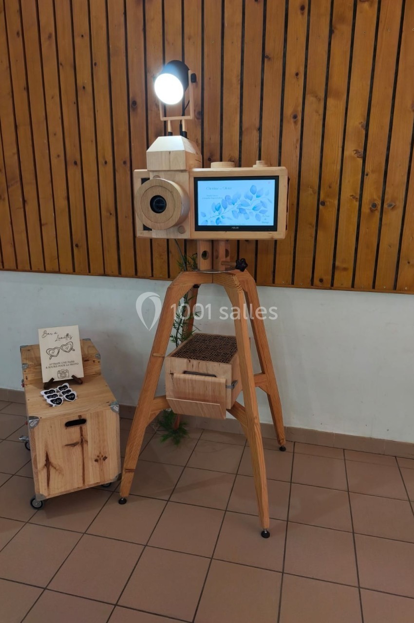 Borne photo en bois avec écran, appareil photo et éclairage intégré, installée dans une salle au mur lambrissé.