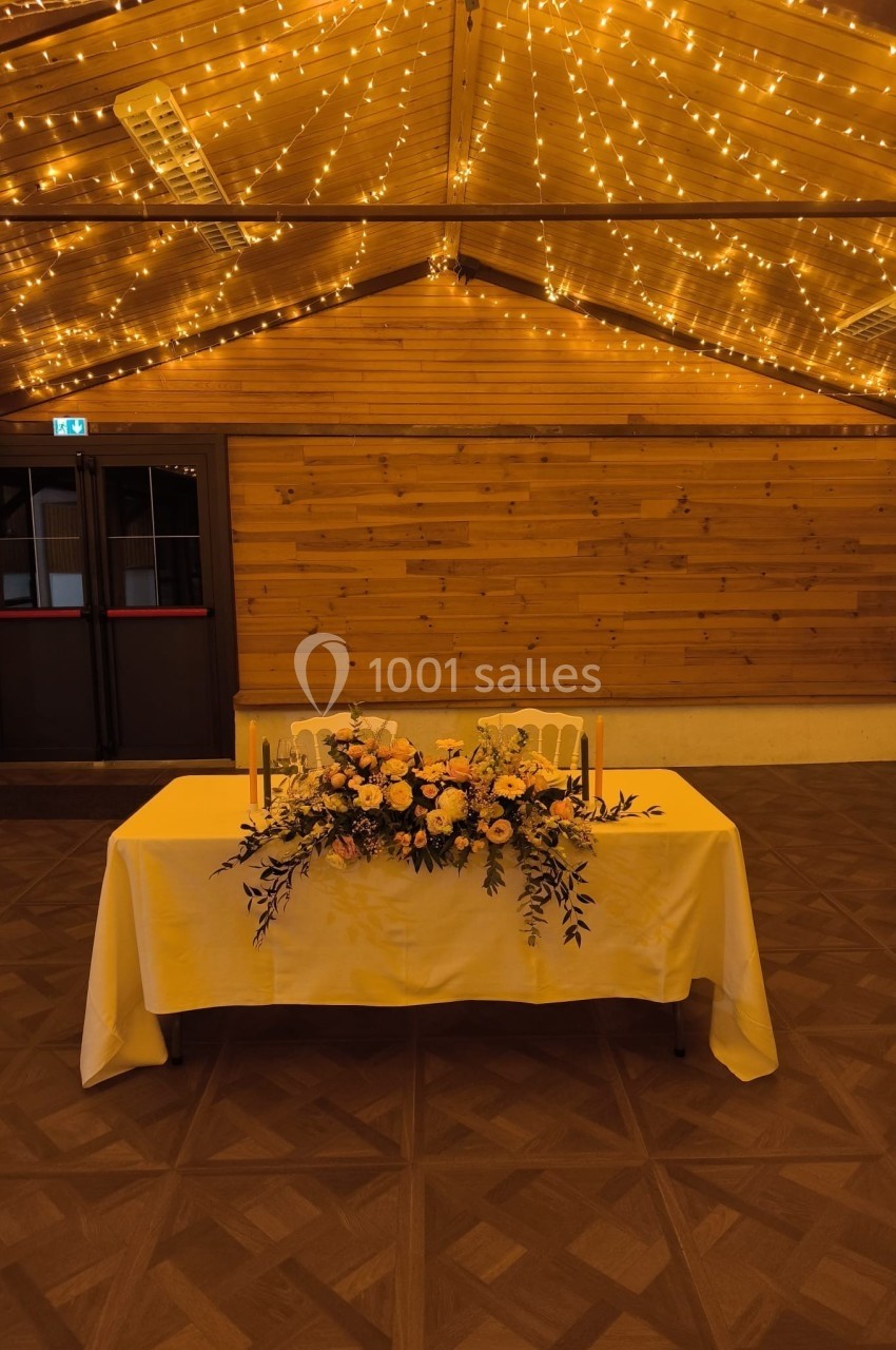 Table décorée avec un bouquet de fleurs jaunes et blanches, sous un plafond illuminé de guirlandes lumineuses.