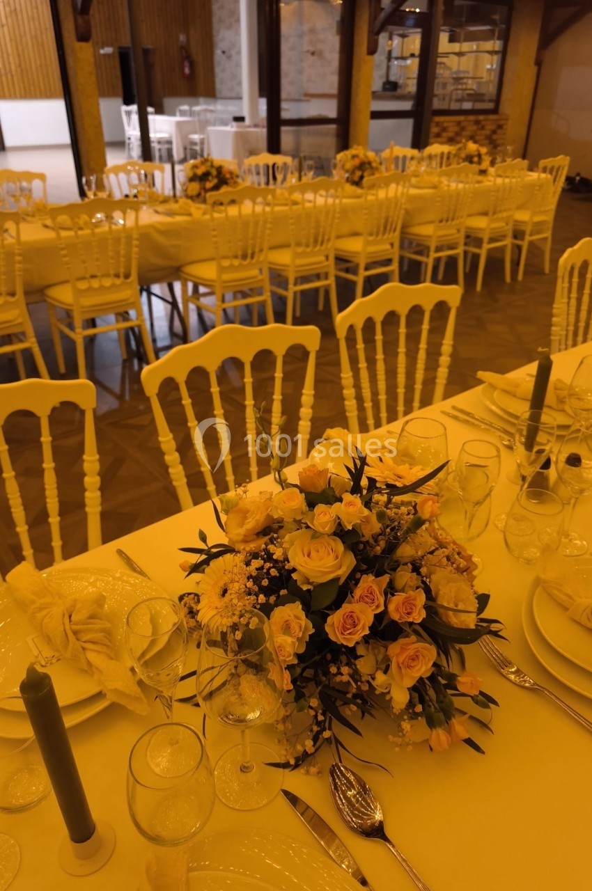 Salle de réception décorée avec des tables dressées, ornées de bouquets de fleurs jaunes et blanches.