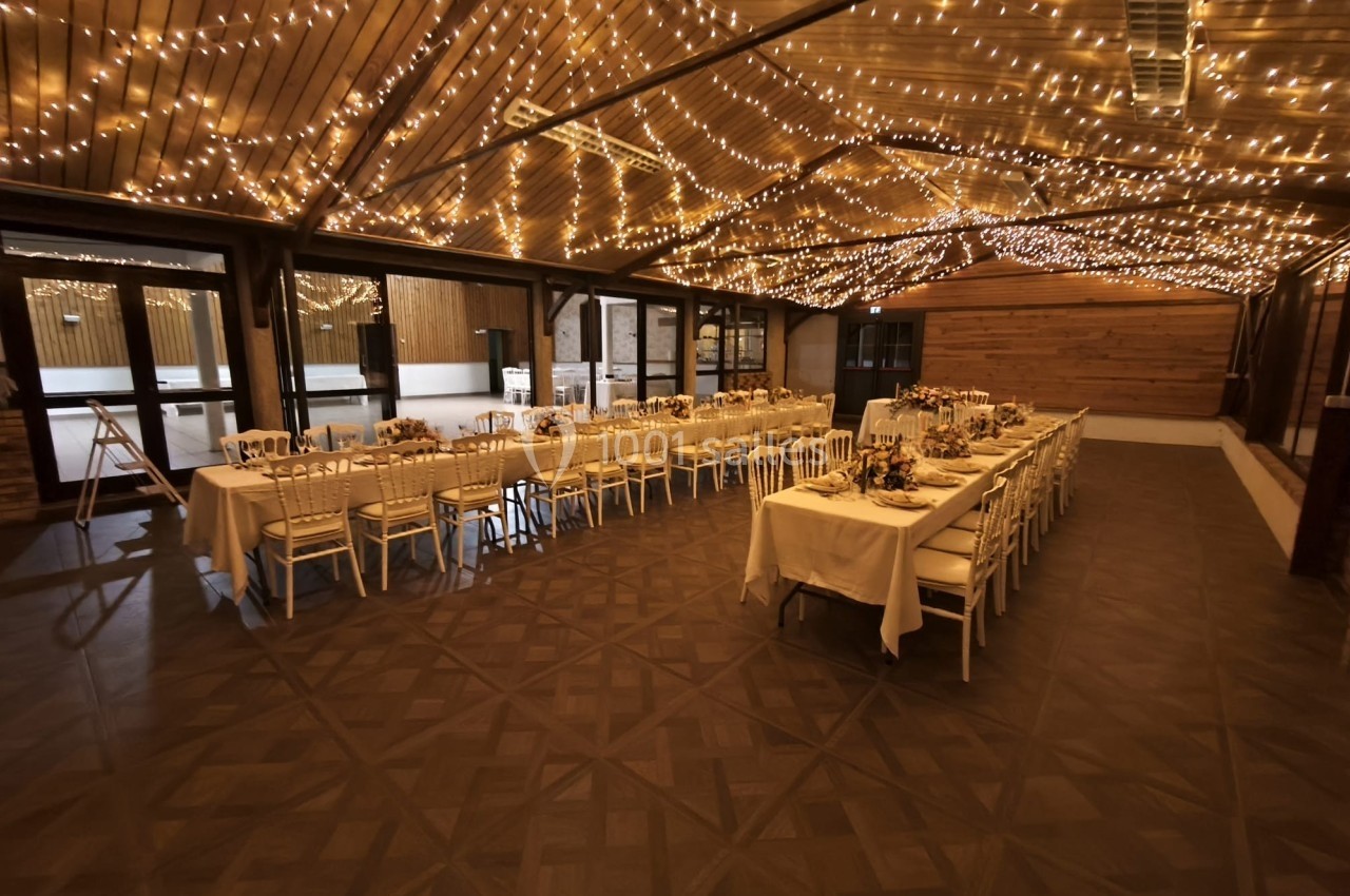 Salle de réception décorée avec des guirlandes lumineuses suspendues et des tables dressées pour un repas.