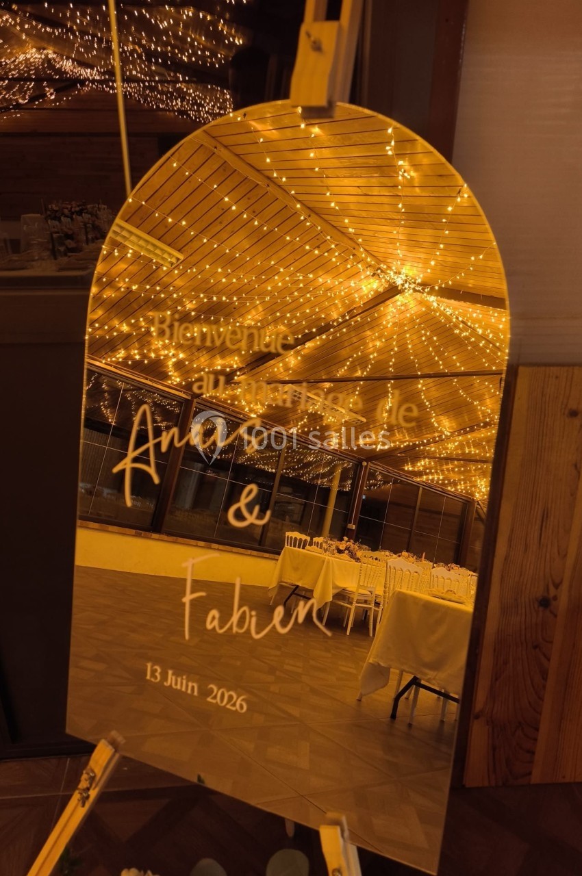 Miroir doré avec inscription personnalisée pour un mariage, reflétant une salle décorée de guirlandes lumineuses.