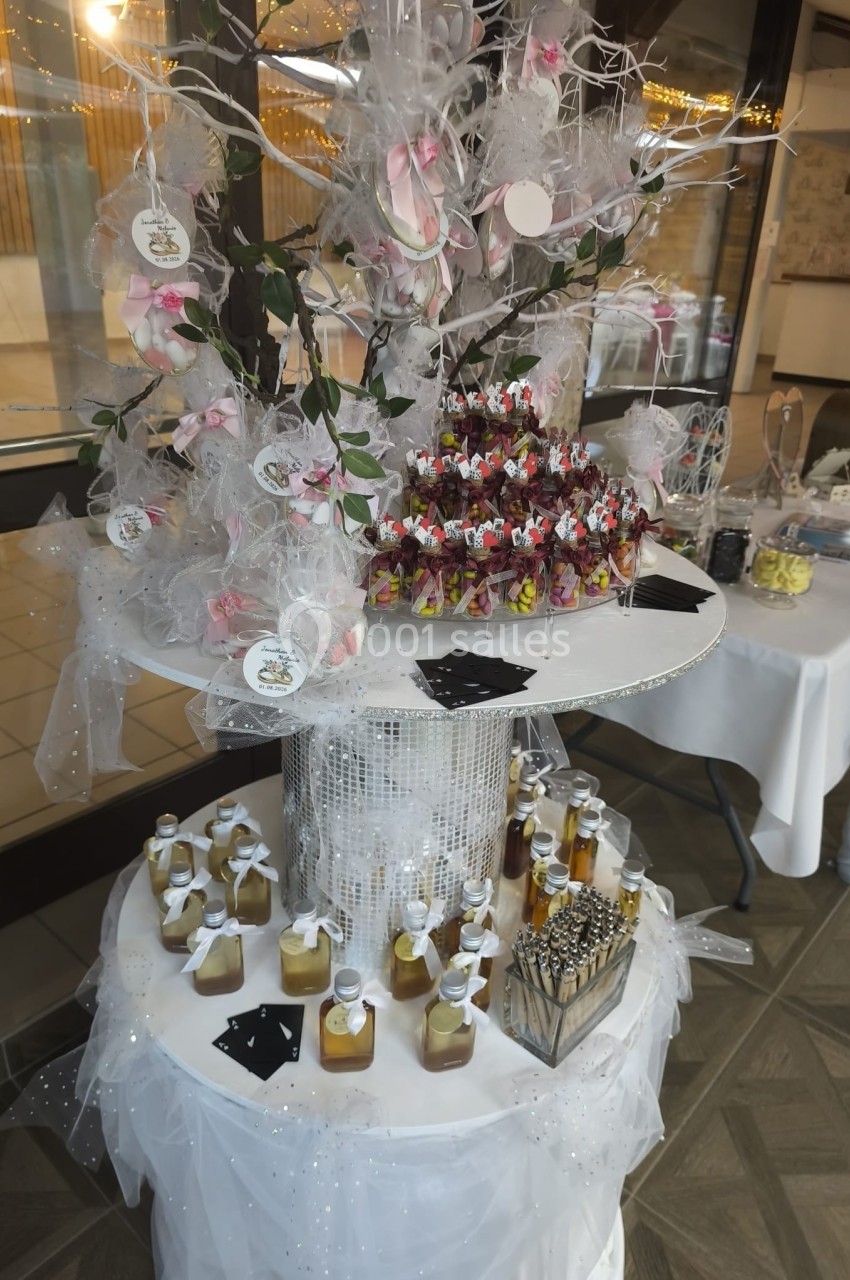 Table décorative avec un arbre orné de rubans et fleurs, entouré de petits cadeaux et flacons pour un événement festif.