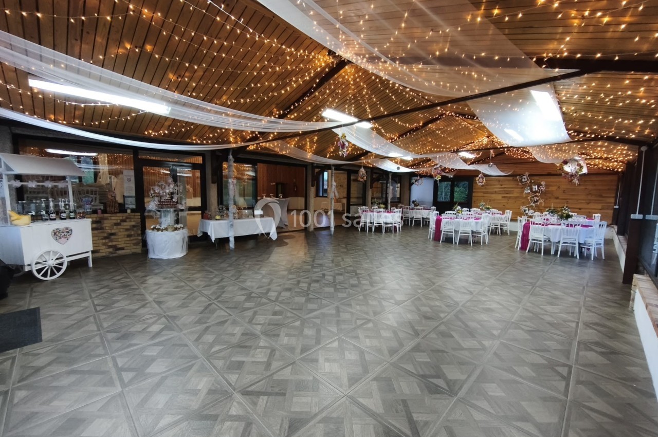 Salle de réception décorée avec des guirlandes lumineuses et des tables dressées pour un événement festif.