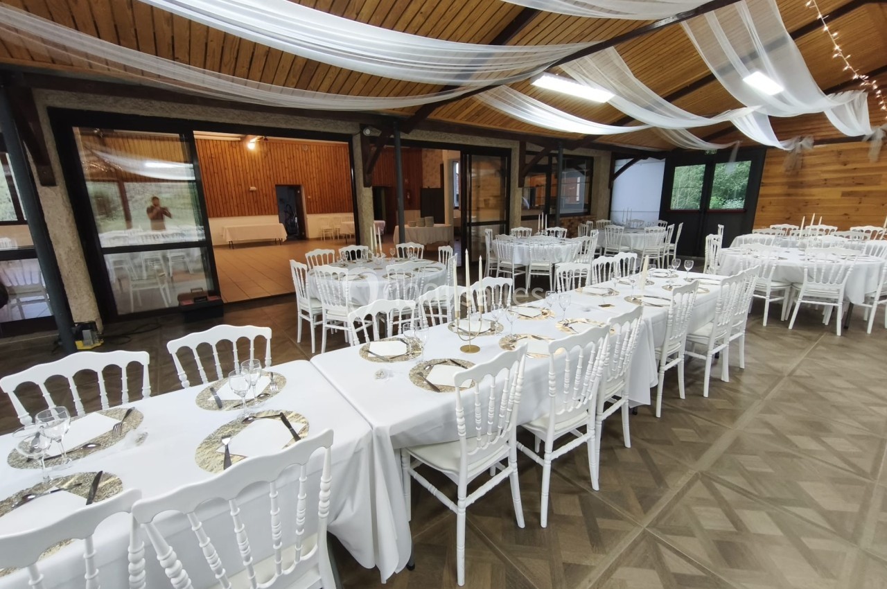 Salle de réception décorée avec des tables dressées, nappes blanches et chaises en bois blanc sous un plafond orné de…