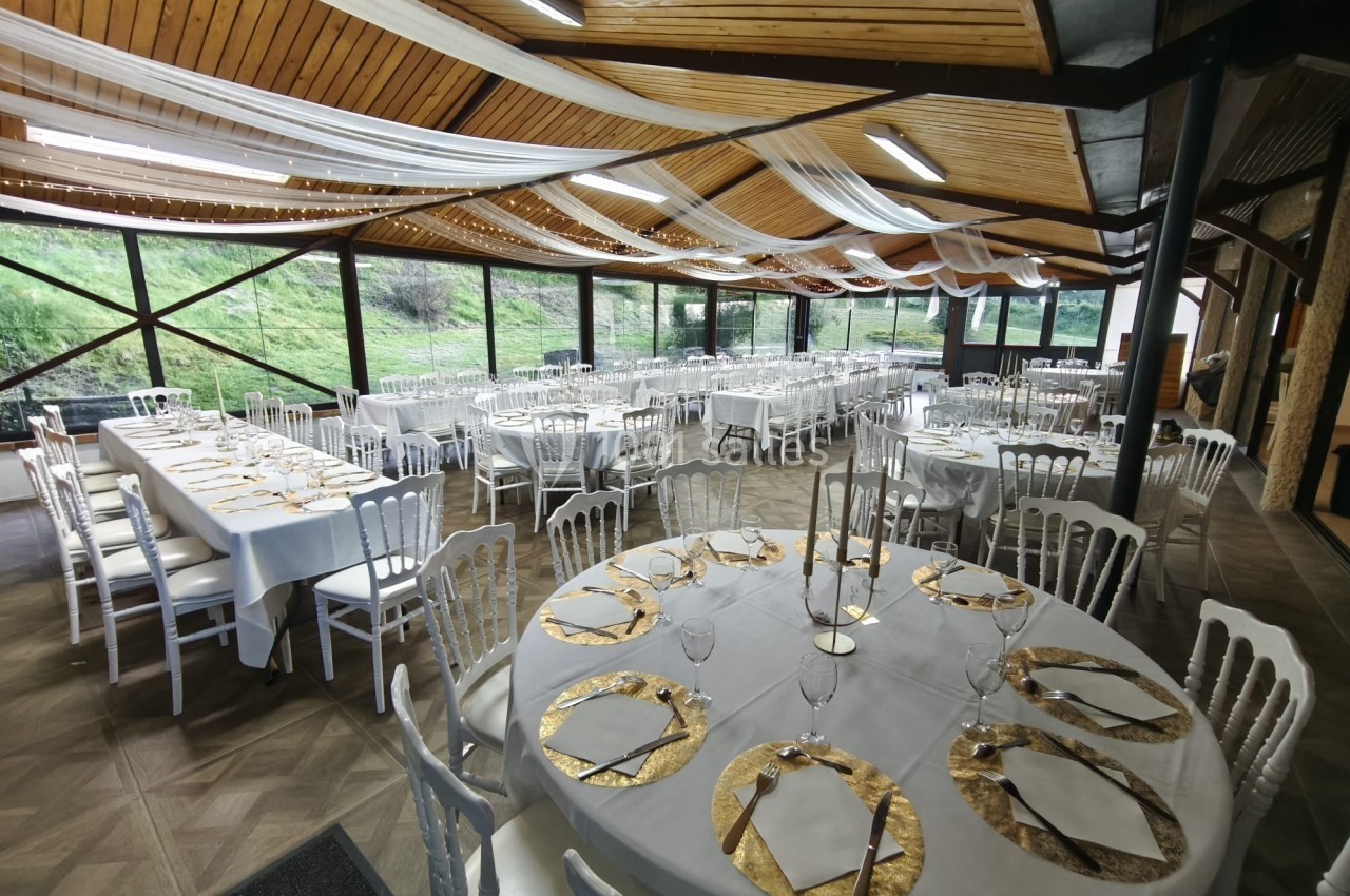 Salle de réception décorée avec des tables rondes et rectangulaires dressées, ornées de nappes blanches et détails dorés.