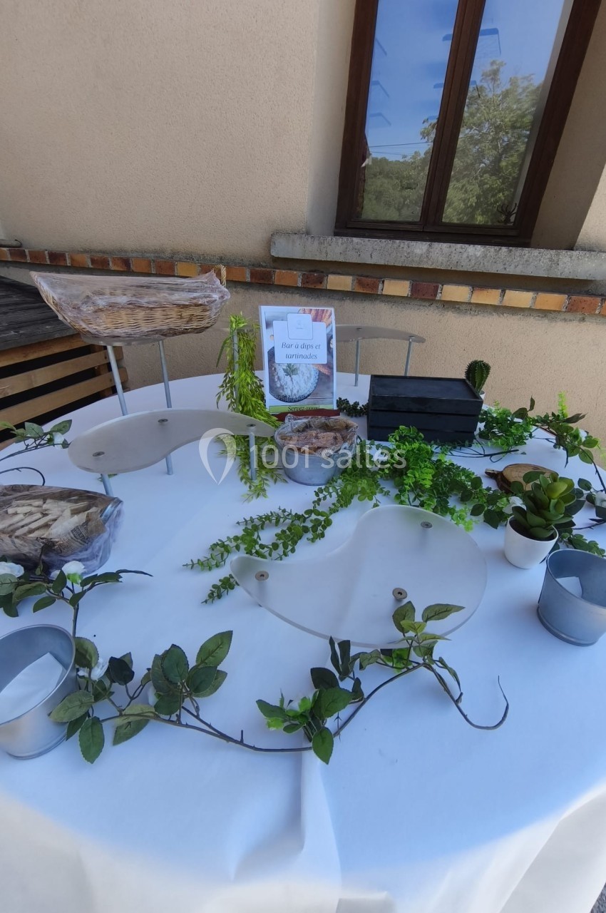 Table dressée en extérieur avec nappage blanc, décorations végétales et présentoirs contenant des aliments.
