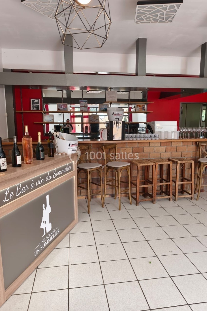 Intérieur d'un bar à vin avec comptoir en briques, tabourets hauts, bouteilles exposées et décor moderne.