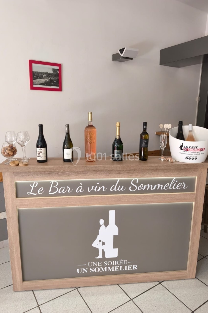 Comptoir de bar avec plusieurs bouteilles de vin exposées, seaux à glace et décoration sobre en arrière-plan.