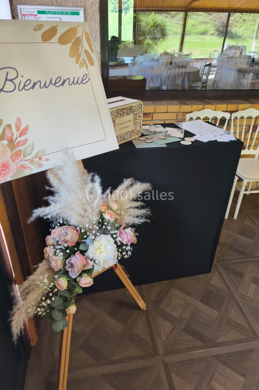 Panneau ’Bienvenue’ décoré de fleurs, posé sur un chevalet près d'une table d'accueil dans une salle lumineuse.
