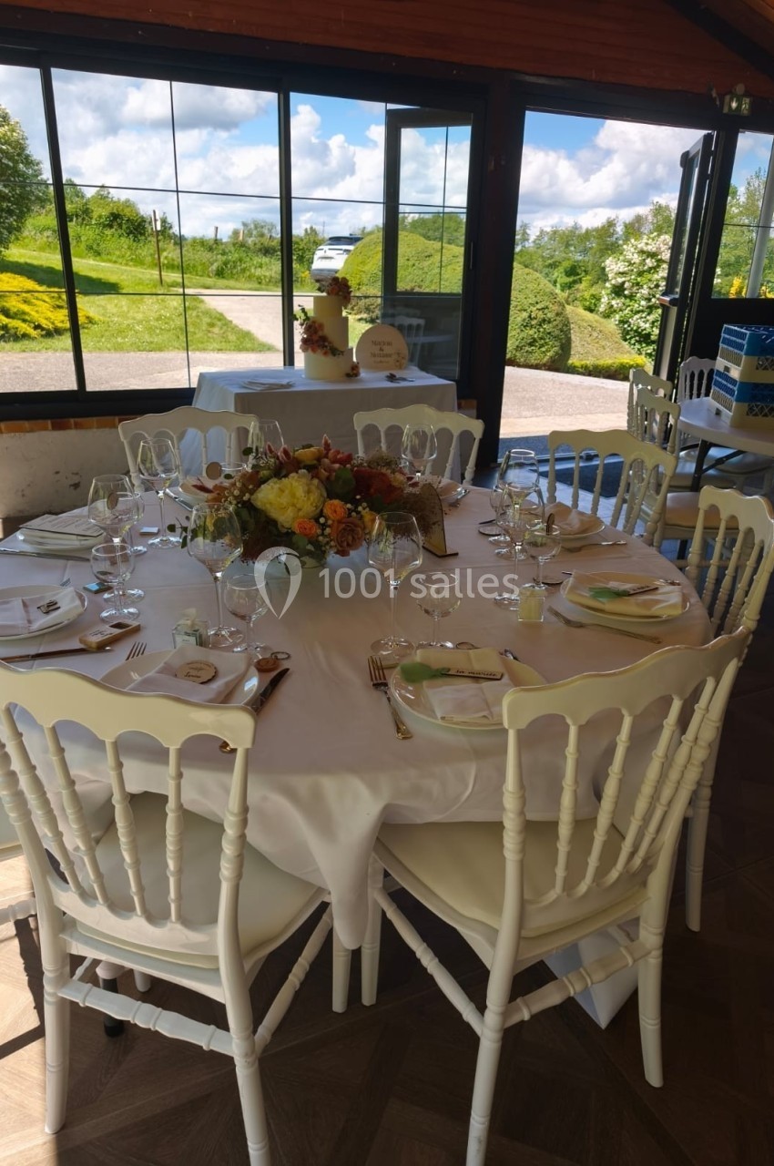 Table ronde dressée pour un repas, décorée avec un centre de table floral, dans une salle lumineuse avec vue sur jardin.