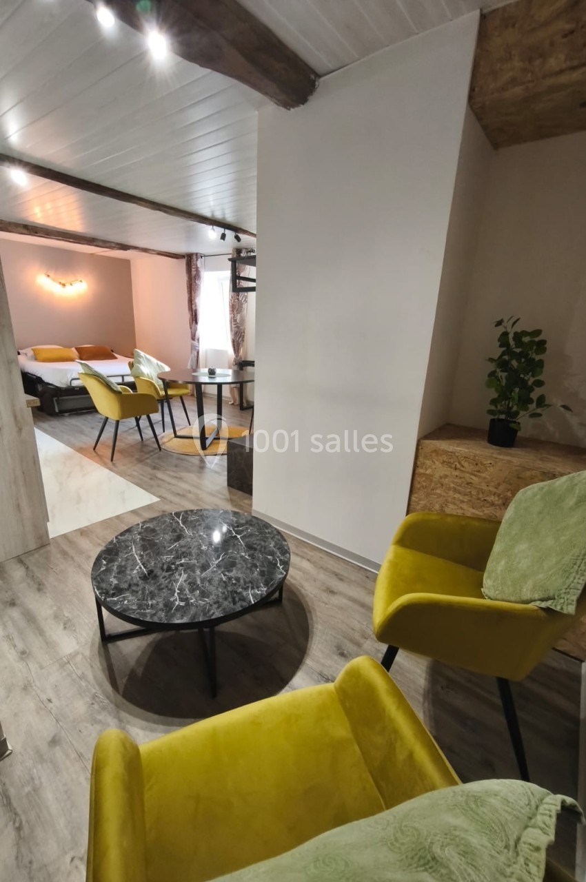 Deux fauteuils jaunes autour d'une table basse en marbre noir dans un espace lumineux avec vue sur une chambre.