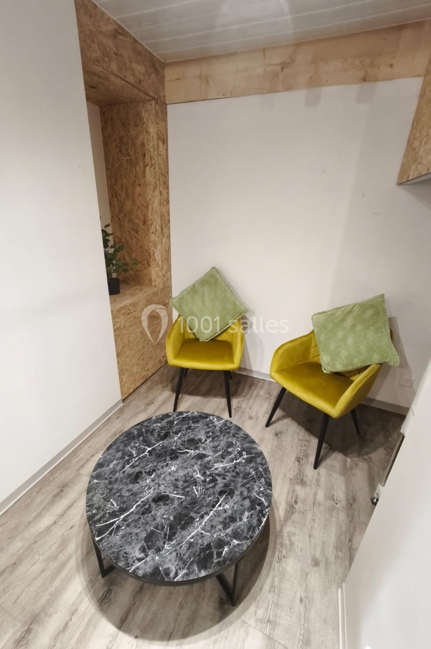Deux fauteuils jaunes avec coussins verts autour d'une table basse ronde en marbre noir, dans un espace moderne.