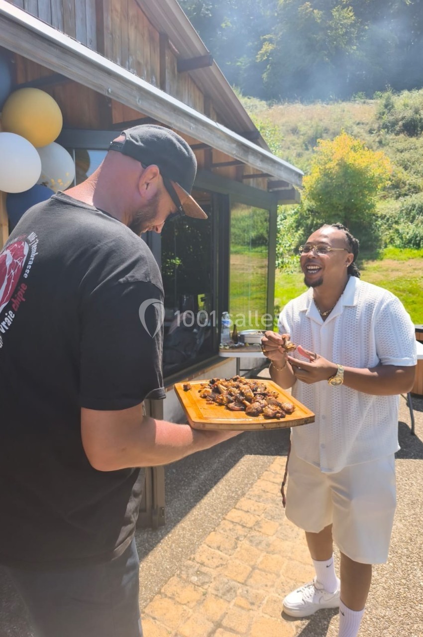 Un homme tend un plateau de grillades à un autre homme souriant lors d'un rassemblement en extérieur.