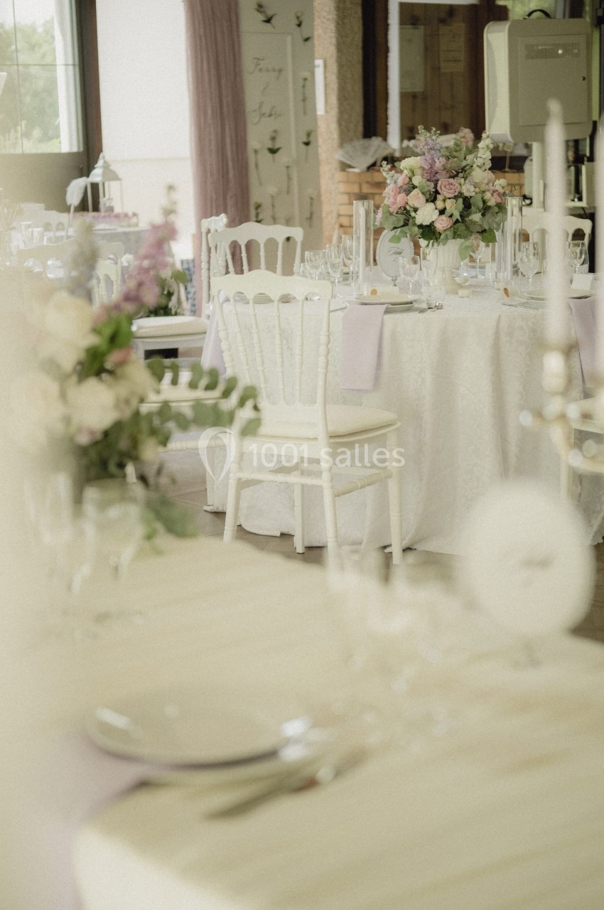 Salle de réception décorée pour un mariage avec tables rondes, nappes blanches, chaises élégantes et bouquets de fleurs.