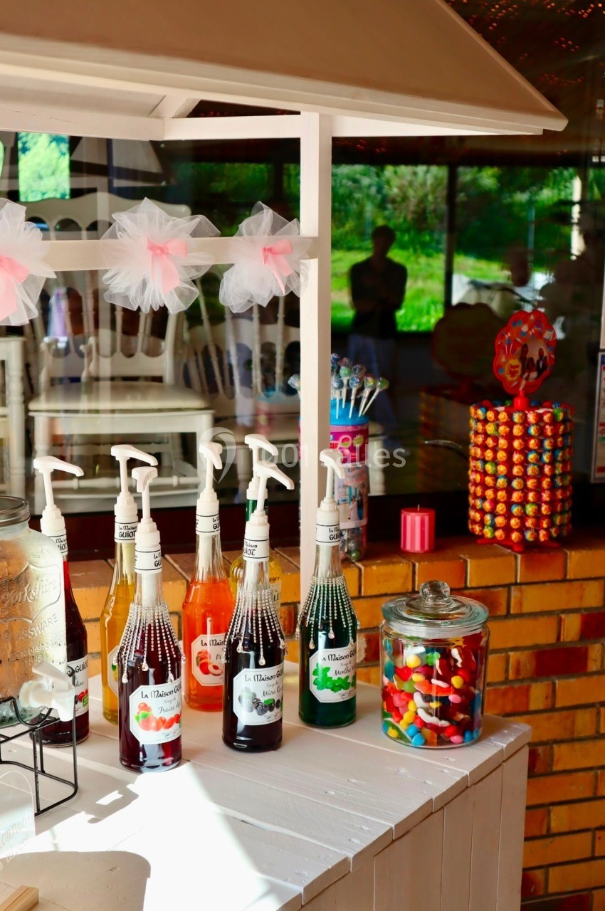 Stand avec sirops, bonbons colorés en bocaux et distributeur de chewing-gums, installé en extérieur lumineux.