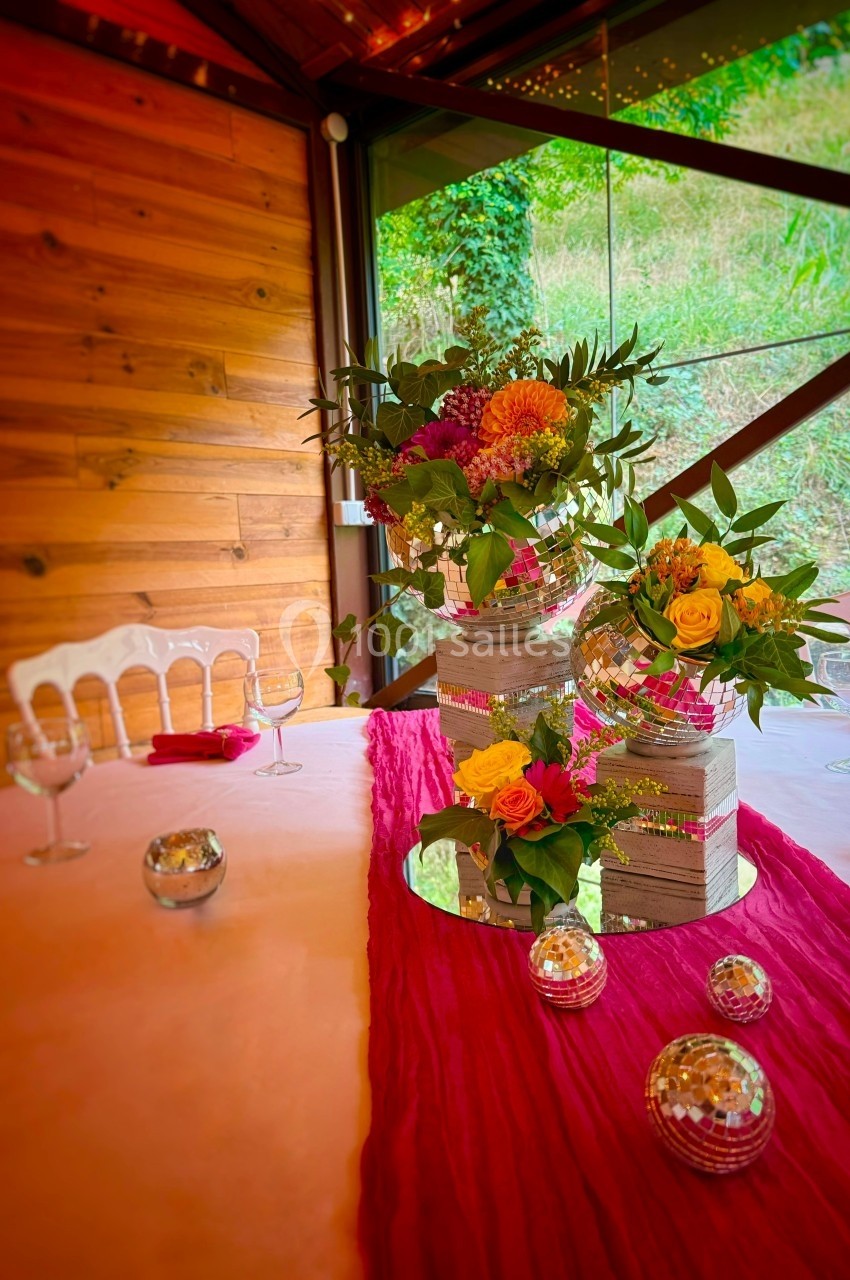 Table décorée avec des fleurs colorées, des miroirs et des boules à facettes, dans une salle avec vue sur un jardin.