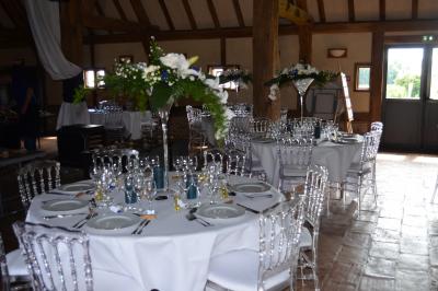 Table ronde élégamment dressée avec nappes blanches, verres, couverts, pains et décoration florale dans une salle de…