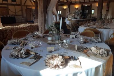 Table ronde élégamment dressée avec nappes blanches, verres, couverts, pains et décoration florale dans une salle de…