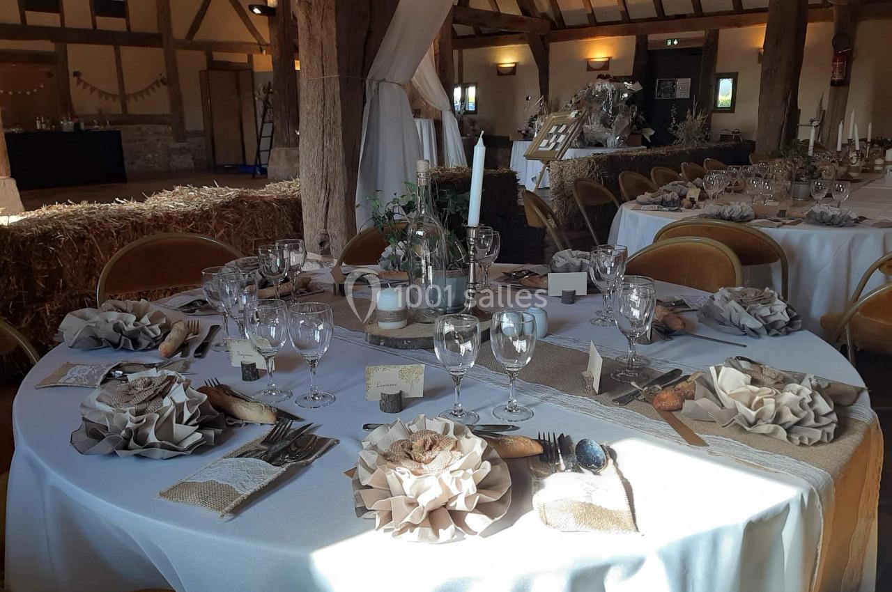 Salle de réception décorée dans un style rustique avec tables rondes dressées et ornées de centres de table naturels.