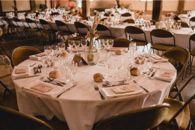 Table ronde élégamment dressée avec nappes blanches, verres, couverts, pains et décoration florale dans une salle de…