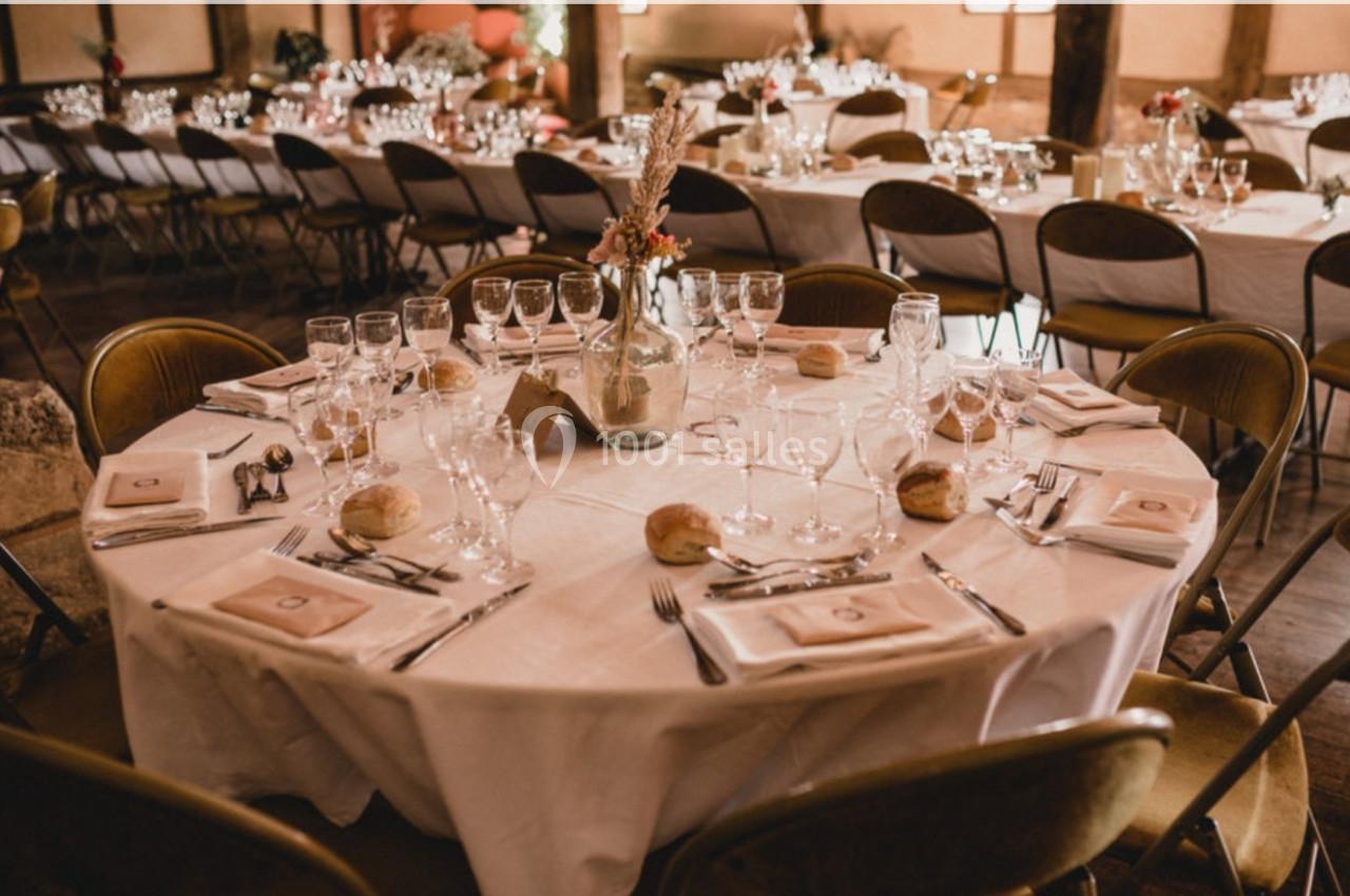 Table ronde élégamment dressée avec nappes blanches, verres, couverts, pains et décoration florale dans une salle de…