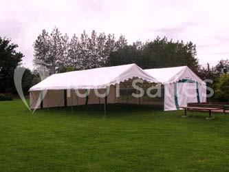 Tente blanche installée sur une pelouse, entourée d'arbres en arrière-plan.