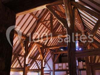 Charpente en bois apparente d'un bâtiment, avec poutres et chevrons visibles sous un éclairage intérieur.