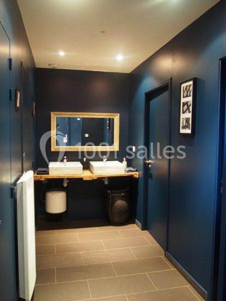 Salle de bain moderne avec murs bleu foncé, deux lavabos sur planche en bois, miroir doré et éclairage encastré.