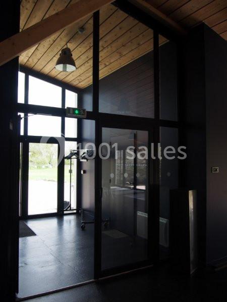 Entrée vitrée avec plafond en bois, porte automatique et vue sur l'extérieur verdoyant.