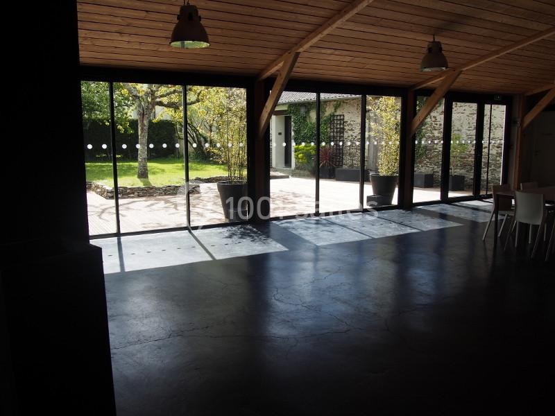Salle intérieure avec sol en béton, grandes baies vitrées donnant sur un jardin ensoleillé avec arbres et terrasse.