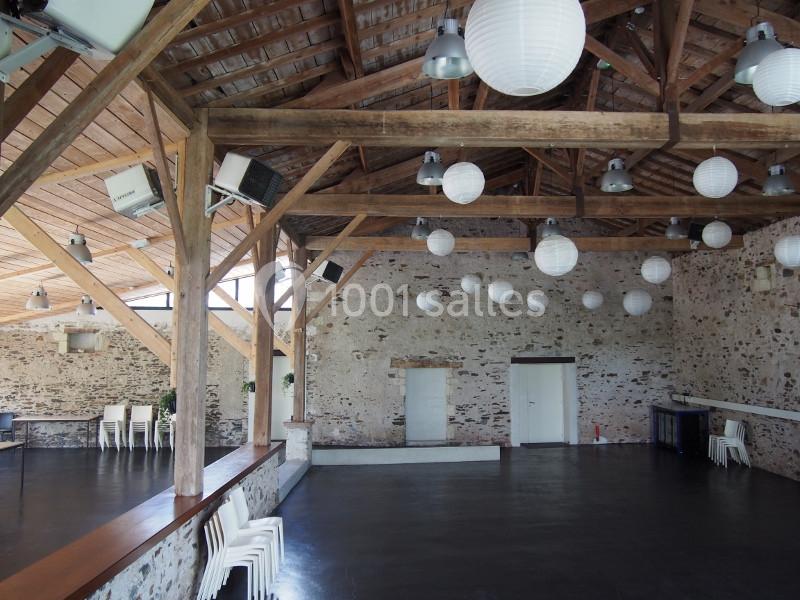 Salle spacieuse avec charpente en bois apparente, murs en pierre et lampions suspendus au plafond.