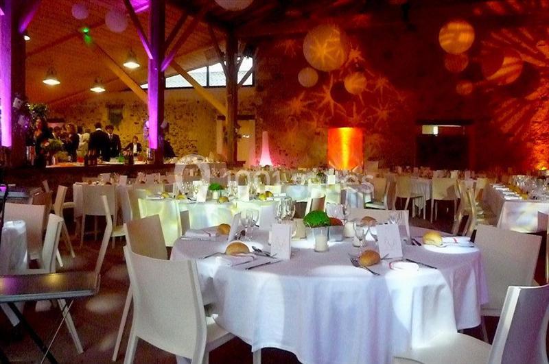 Salle de réception décorée avec des tables rondes dressées, éclairage coloré et ambiance festive.